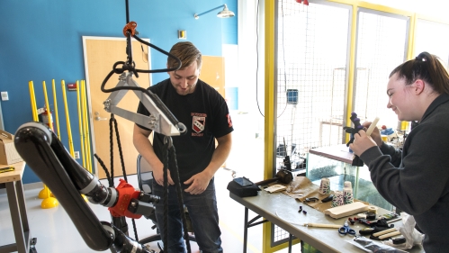 Male and female white students work in a lab with mechanical equipment.