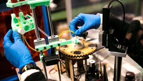 Blue gloved hands manipulate a 3D printer.