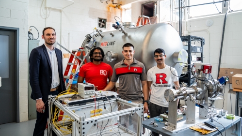 Professor and three male students pose in a lab filled with equipment.