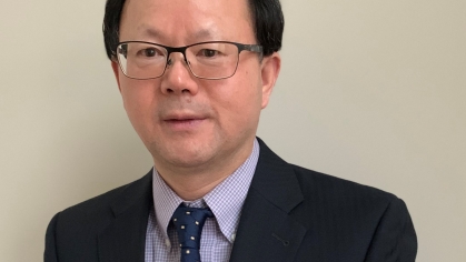 Headshot of white male with grey hair, glasses, wearing a dark suit, white shirt and red tie.