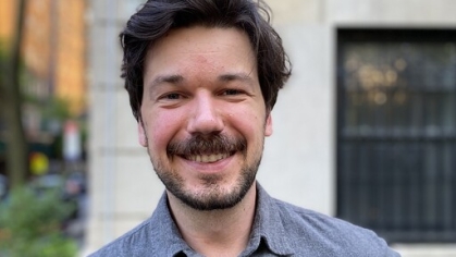 Graduate student poses outside for a headshot. He's wearing a blue collared shirt. He has black hair and a beard.