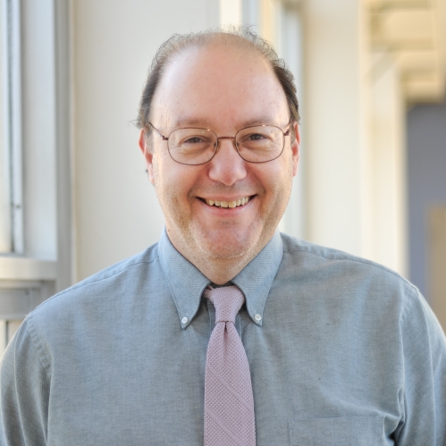 Head shot of balding male with eyeglasses, wearing a pale blue button down shirt and a pink tie.