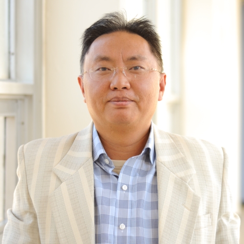Head shot of Asian male with eyeglasses, wearing a light tan suit jacket and a patterned blue shirt.