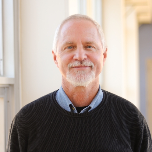 Head shot of male with white hair, beard, and a moustache, wearng a dark pullover sweater.