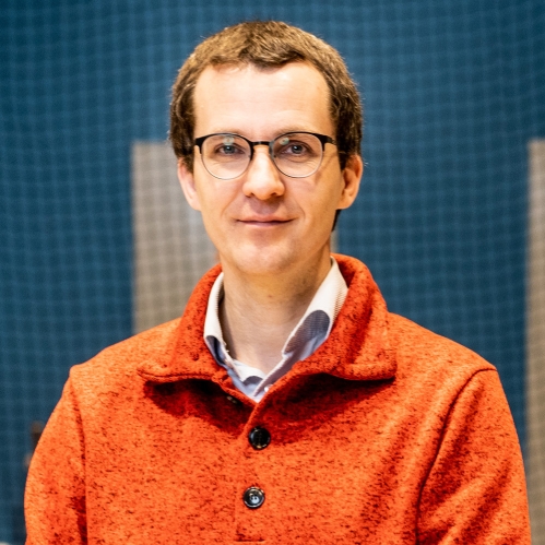 Head shot of male with eyeglasses wearing an orange collared pullover with buttons.
