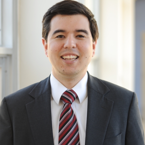 Headshot of male with dark brown hair, wearing a suit and tie.