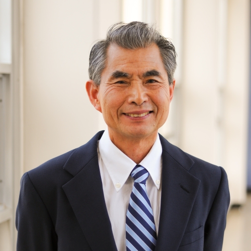 Head shot of Asian male wearing a black suit with white shirt and a patterned tie.