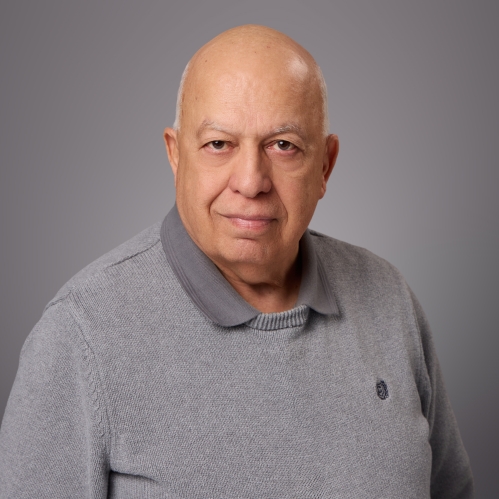 Headshot of bald male wearing a grey polo shirt underneath a grey pullover sweater.