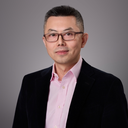 Headshot of male with short black hair and eyeglasses wearing a pink button down shirt and a black suit jacket.