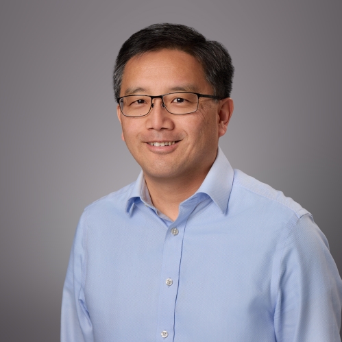 Headshot of male with short black hair and eyeglasses wearing a blue button down dress shirt.