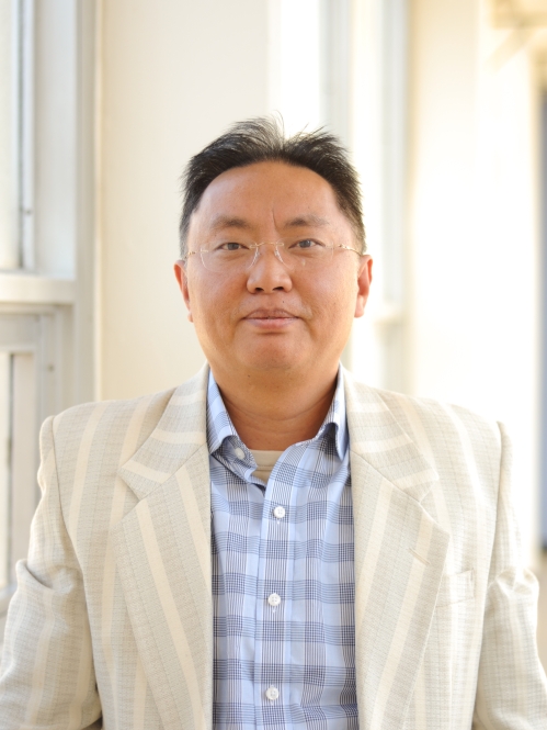 Head shot of Asian male with eyeglasses, wearing a light tan suit jacket and a patterned blue shirt.