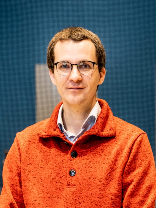 Head shot of male with eyeglasses wearing an orange collared pullover with buttons.