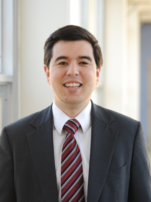 Headshot of male with dark brown hair, wearing a suit and tie.