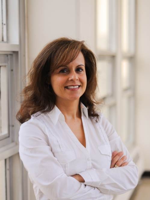 Head shot of female with her arms folded with long brown hair, wearing a white blouse