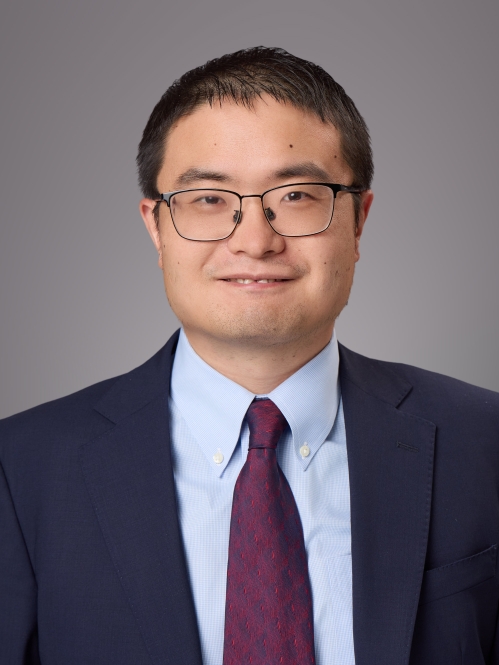 Headshot of male with short black hair and eyeglasses wearing a dark blue suit jacket, a light blue button down shirt, and a burgundy tie.