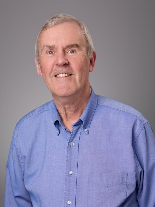 Headshot of male with short white hair wearing a blue button down shirt.