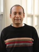 Head shot of male with eyeglasses and short hair, wearing a black pullover sweater.
