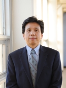 Head shot of Chinese male with short black hair, wearing a black suit, blue shirt, and patterned blue tie.