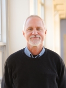 Head shot of male with white hair, beard, and a moustache, wearng a dark pullover sweater.