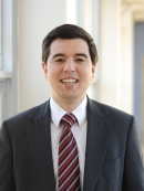 Headshot of male with dark brown hair, wearing a suit and tie.