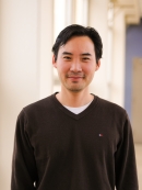 Head shot of Asian male wearing a dark brown pullover sweater.