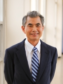Head shot of Asian male wearing a black suit with white shirt and a patterned tie.