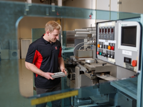 A male student works with industrial equipment that has controls and other mechanics.