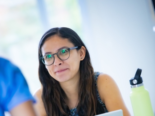 White female college student with brown hair and glasses working on a laptop.
