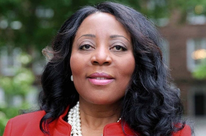Headshot of an African American woman with black shoulder length wearing a red suit jacket with a white pearl necklace.