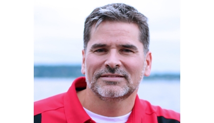 Headshot of white male with a beard and moustache wearing a red and black pullover.