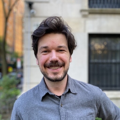 Graduate student poses outside for a headshot. He's wearing a blue collared shirt. He has black hair and a beard.