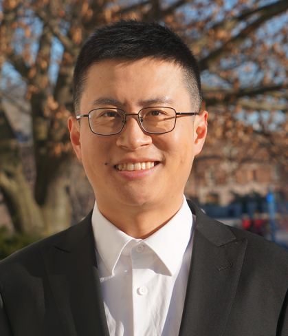 Headshot of Asian man with short dark hair wearing glasses, a dark suit jacket and white shirt