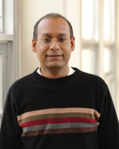 Head shot of male with eyeglasses and short hair, wearing a black pullover sweater.