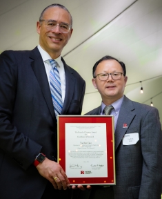 Two men pose with award certificate. Taller man on left presents the award.
